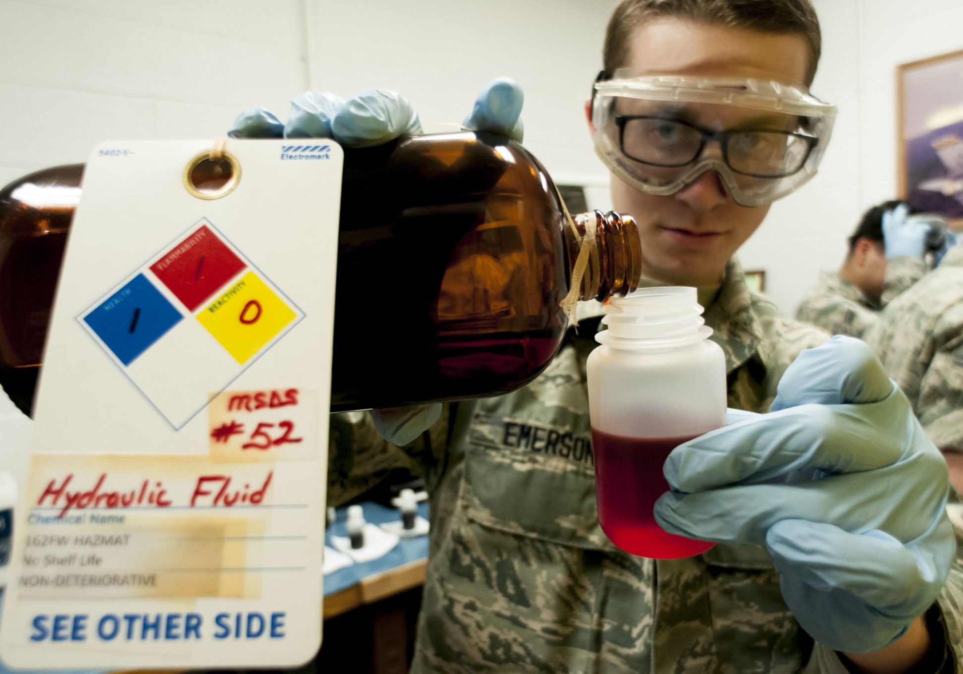 female airman wearing goggles, carefully pouring chemicals
